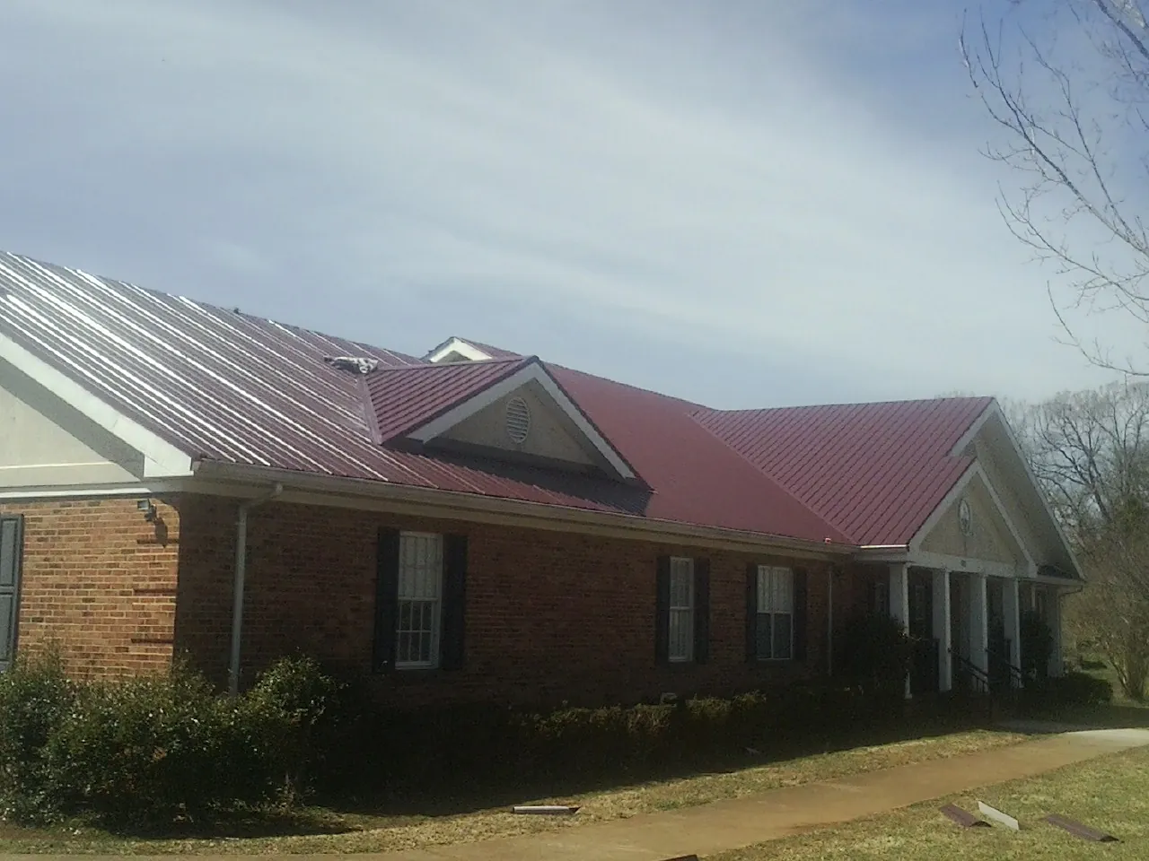 Red metal roof with gabled entries on a long brick building, from a Hail Damage Roof Repair job in Griffin