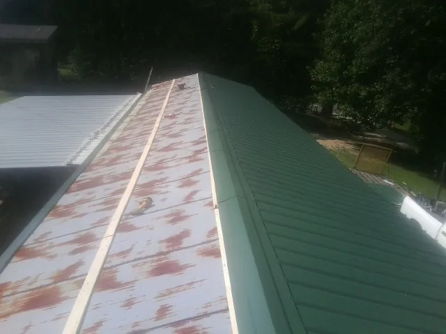 Old rusted panels beside newly installed green metal roofing — Wind Damage Roof Repair by Roofing Brothers in Griffin