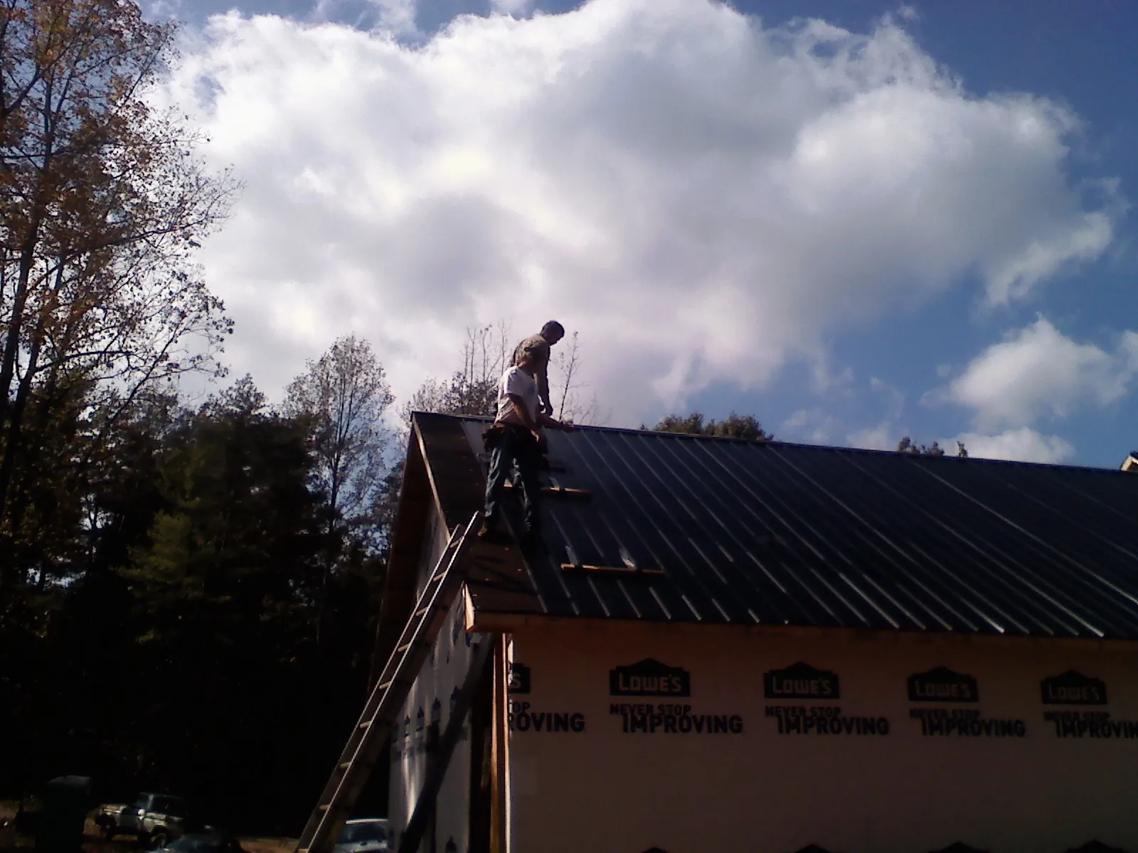 Roofer fastening dark metal panels high against a cloudy sky, from a Roof Inspection job in Griffin