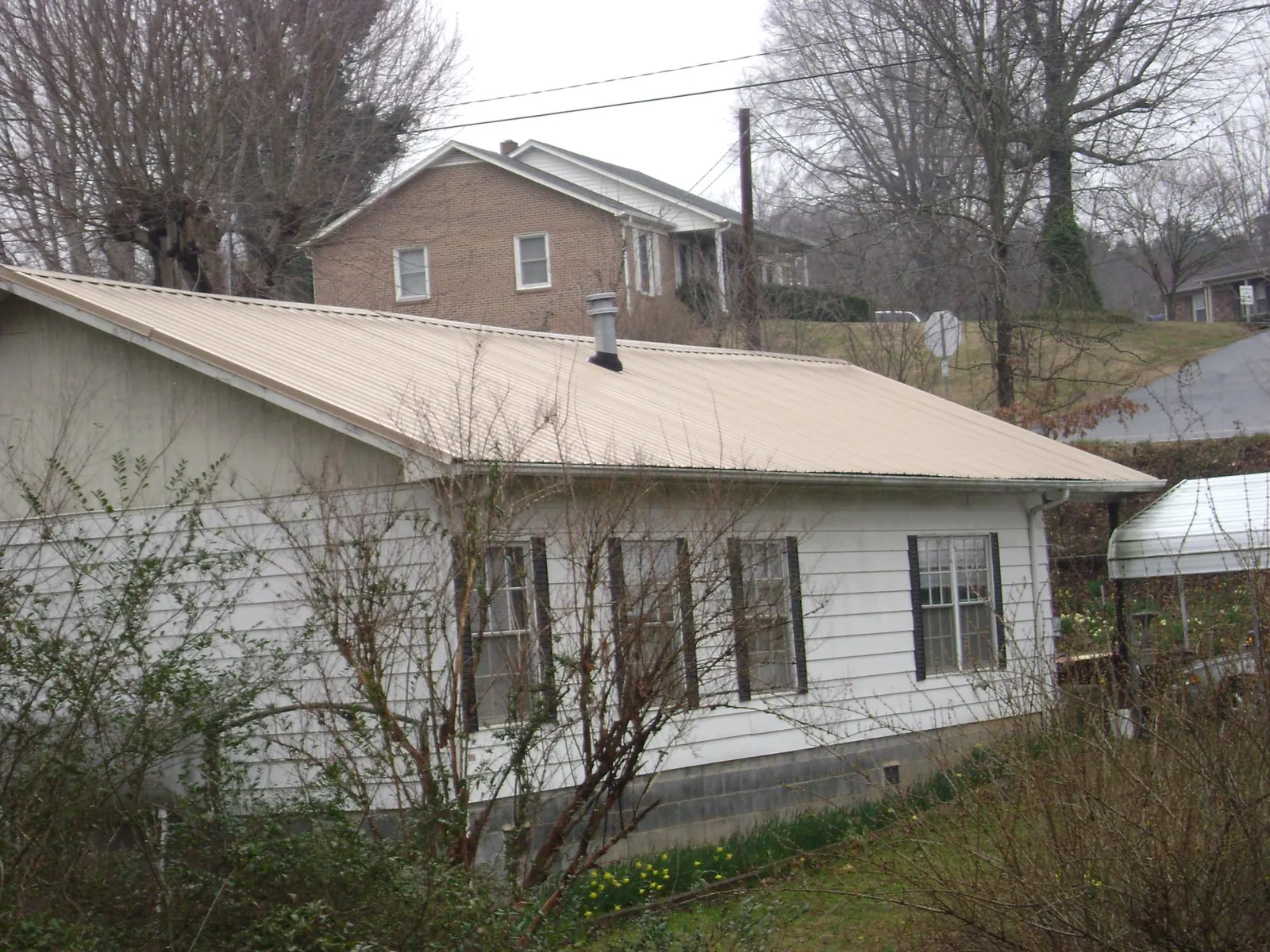 Tan metal roof on a white sided house set into a hillside — Commercial Roofing by Roofing Brothers in Griffin